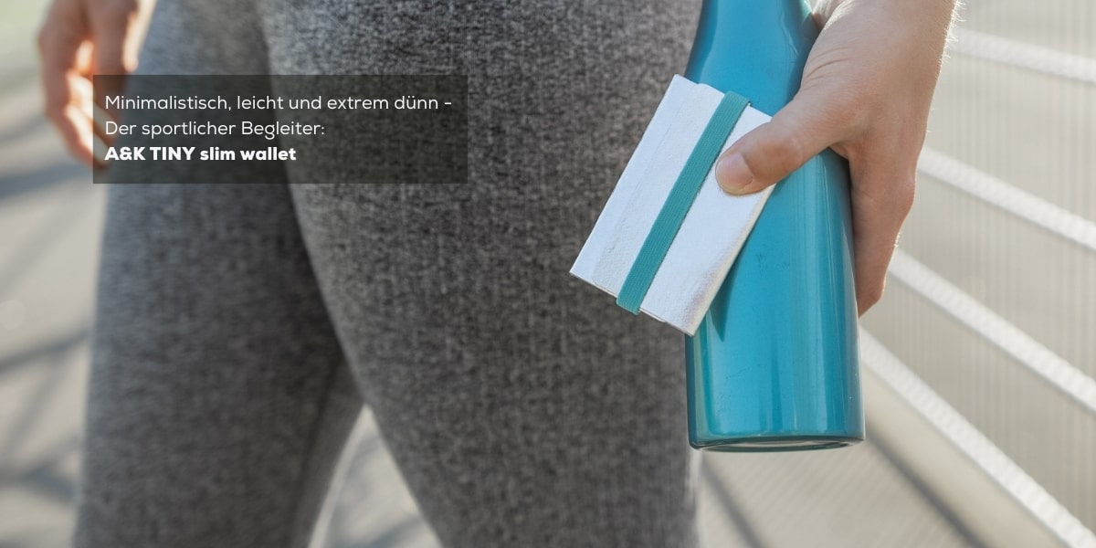 TINY Wallet in Silber Mint wird von einer Frau gehalten, die eine Sporthose trägt und eine türkisfarbene Flasche in der Hand hält. Dies veranschaulicht die kleine, leichte und schlanke Bauweise des A&K TINY Wallets.